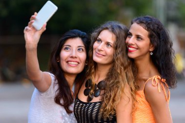 Portrait of three young beautiful women as friends together in the streets outdoors