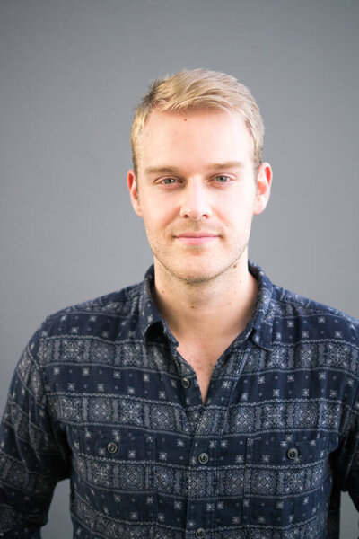 Portrait of young handsome businessman with blond hair against gray background