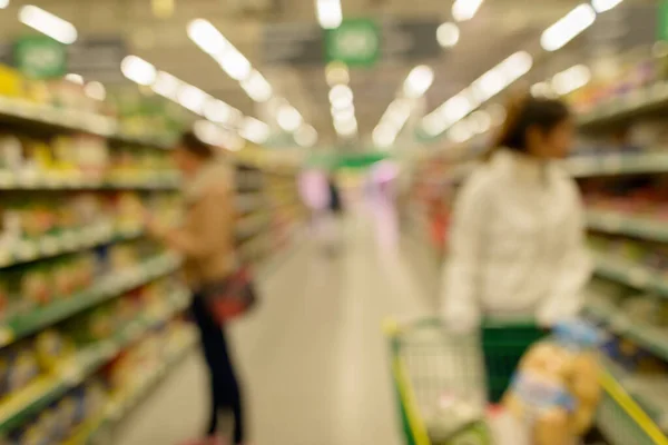 Portrait of blurred customers shopping for groceries in supermarket loaded with variety of products on shelves