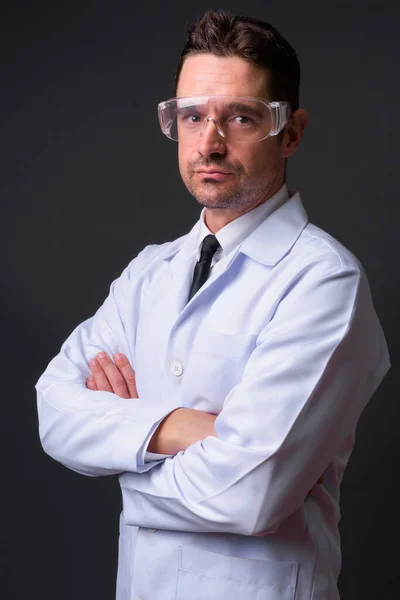 长胡子英俊男医生作为科学家配戴灰色背景防护眼镜的摄影棚照片 — 图库照片