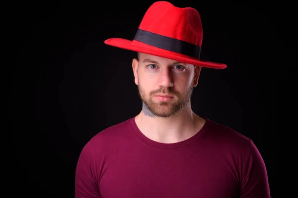 スタジオショットのハンサムなひげを生やした男を身に着けています赤フェドーラ帽子に対して黒背景 — ストック写真