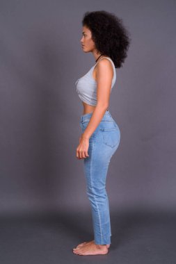 Gri arka planda Afro saçlı çok ırklı Afrikalı Amerikalı genç bir kadının stüdyo fotoğrafı.