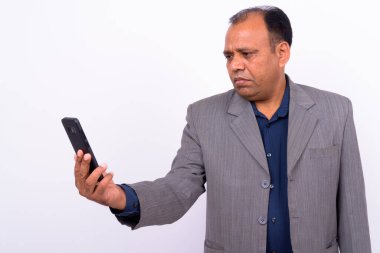 Takım elbiseli olgun Hintli işadamının beyaz arka planda saç çizgisinin çekildiği bir stüdyo resmi.
