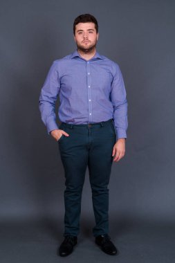 Yakışıklı, şişman, sakallı iş adamının gri arka planda çekilmiş bir fotoğrafı.