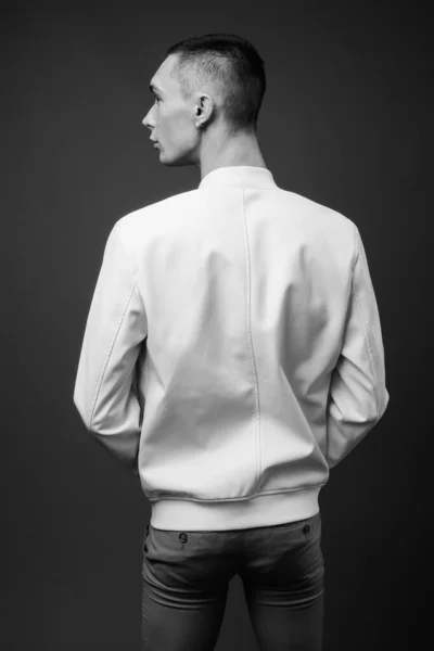 Studio shot of young handsome androgynous man with jacket fully unbuttoned against gray background in black and white