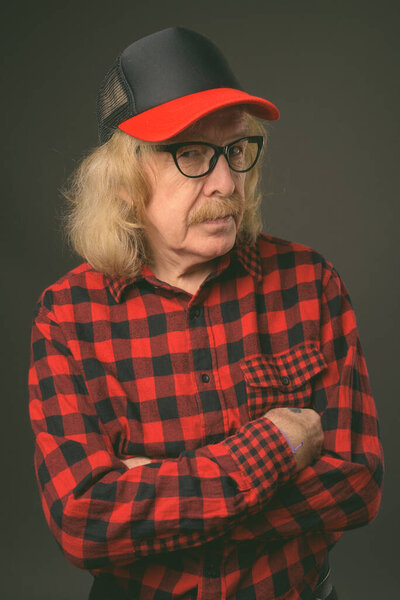 Студийный снимок пожилого человека с усами в кепке и очках на сером фоне