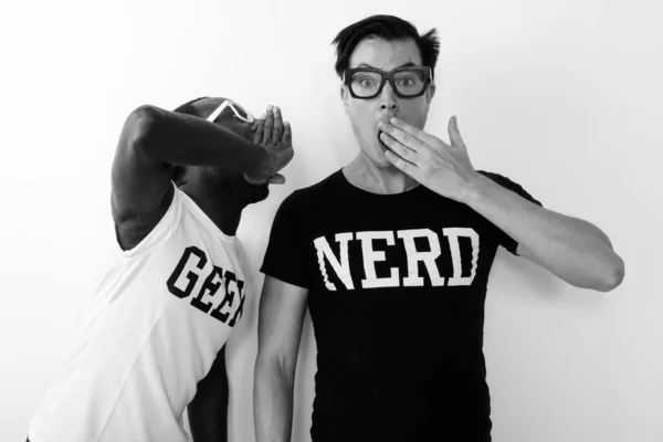 Young African nerd man with young Scandinavian nerd man together against white background in black and white