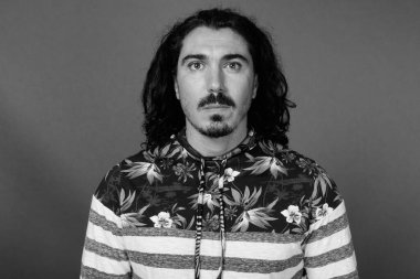 Kıvırcık saçlı, bıyıklı, siyah beyaz arka planlı yakışıklı adamın stüdyo fotoğrafı.