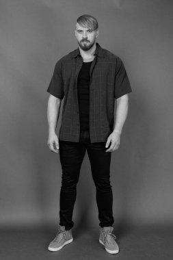 Stüdyo resmi, sarı saçlı, gri arka planda siyah beyaz günlük kıyafetler giyen sakallı adam.