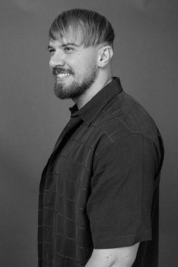 Stüdyo resmi, sarı saçlı, gri arka planda siyah beyaz günlük kıyafetler giyen sakallı adam.