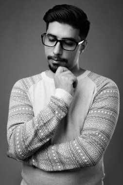 Siyah-beyaz gri arka planda günlük giysiler giyen genç sakallı İranlı adamın stüdyo fotoğrafı.