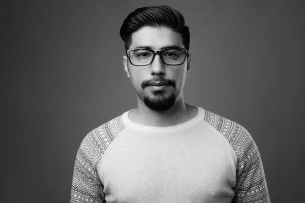 Studio shot of young bearded Iranian man wearing casual clothes against gray background in black and white