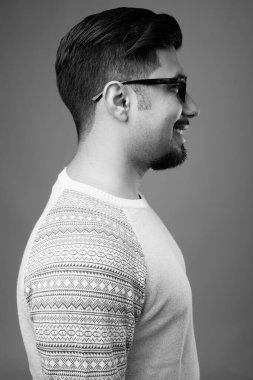 Siyah-beyaz gri arka planda günlük giysiler giyen genç sakallı İranlı adamın stüdyo fotoğrafı.