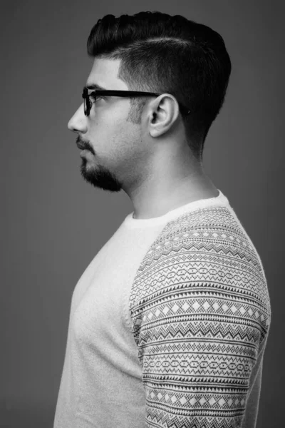 Studio shot of young bearded Iranian man wearing casual clothes against gray background in black and white