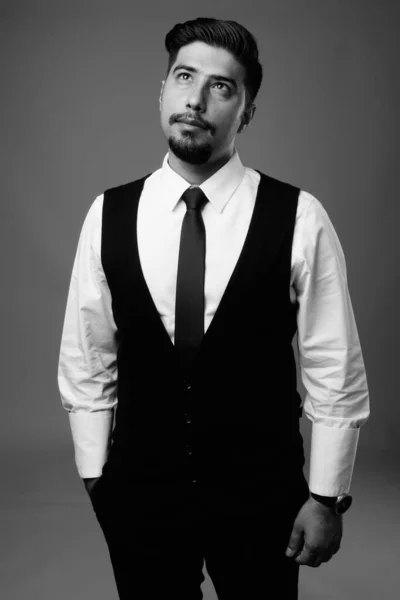 Studio shot of young bearded Iranian businessman against gray background in black and white