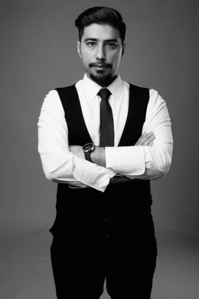 Studio shot of young bearded Iranian businessman against gray background in black and white