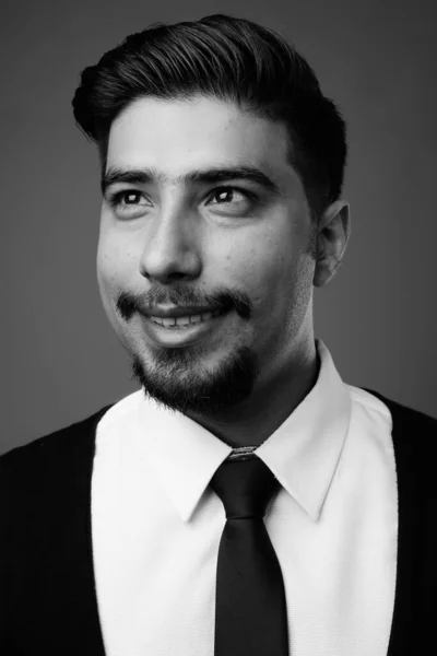 Studio shot of young bearded Iranian businessman against gray background in black and white