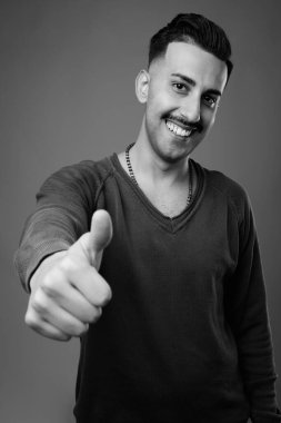 Bıyıklı, uzun kollu, gri arka planlı, siyah beyaz saçlı, yakışıklı İranlı genç adamın stüdyo fotoğrafı.