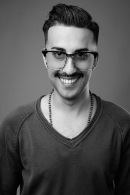 Bıyıklı, uzun kollu, gri arka planlı, siyah beyaz saçlı, yakışıklı İranlı genç adamın stüdyo fotoğrafı.