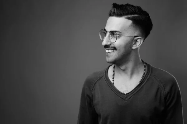 Studio shot of young handsome Iranian man with mustache with long sleeved shirt against gray background in black and white