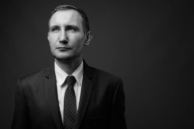 İş adamının gri arka planda siyah beyaz takım elbise giydiği bir fotoğraf.