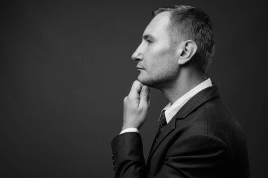 İş adamının gri arka planda siyah beyaz takım elbise giydiği bir fotoğraf.