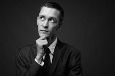 Siyah beyaz gri arka planda takım elbise giyen genç işadamının stüdyo fotoğrafı.