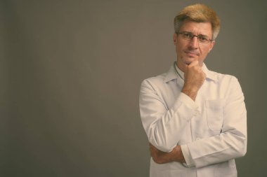 Stüdyo fotoğrafı, sarı saçlı, gri arka planda bir erkek doktor.