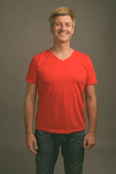 スタジオショットの男とともにブロンド髪身に着けている赤いシャツに対して灰色の背景 — ストック写真