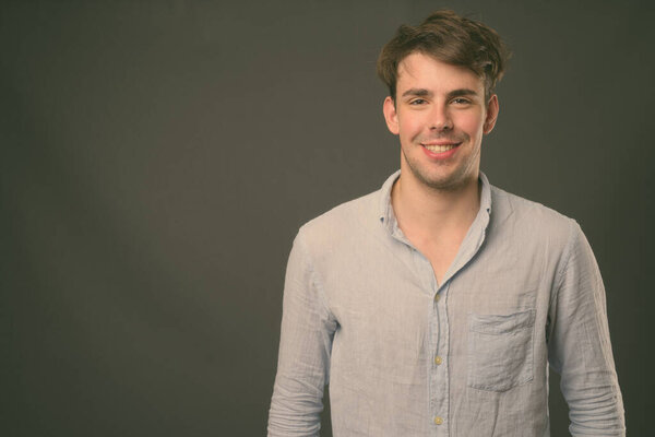 Studio shot of young handsome man wearing blue shirt against gray background