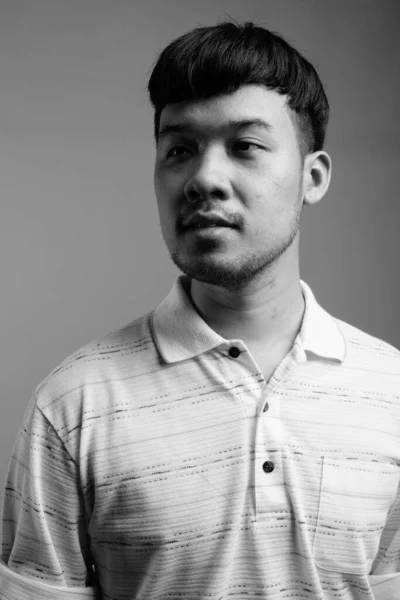 スタジオショットの若いですアジア人男性身に着けていますストライプポロシャツに対してグレー背景で黒と白 — ストック写真