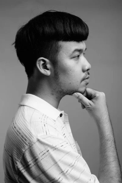 スタジオショットの若いですアジア人男性身に着けていますストライプポロシャツに対してグレー背景で黒と白 — ストック写真