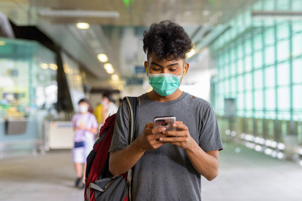 Portrait of young Asian tourist man as backpacker with mask for protection from corona virus outbreak at the sky train station