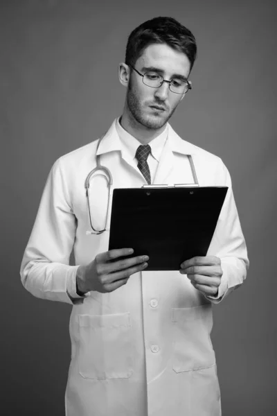 Estudio Joven Guapo Doctor Con Anteojos Sujetando Portapapeles Sobre Fondo — Foto de Stock