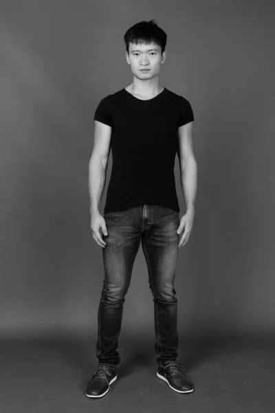 演播室拍摄的年轻中国男子身穿黑色衬衫 背景灰白 黑白相间的照片 — 图库照片