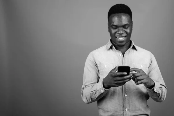 Studio shot of young African man wearing denim shirt against gray background in black and white