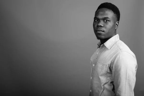 Studio shot of young African man wearing denim shirt against gray background in black and white