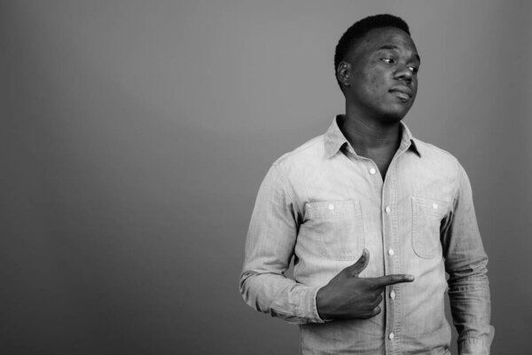 Studio shot of young African man wearing denim shirt against gray background in black and white