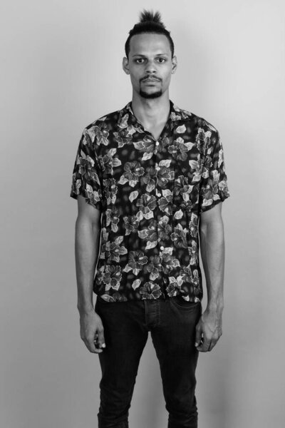 Studio shot of young bearded handsome African man wearing Hawaiian shirt against gray background in black and white