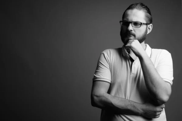 Studio shot of young bearded man wearing white polo shirt against gray background in black and white