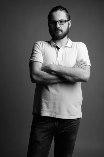 Studio shot of young bearded man wearing white polo shirt against gray background in black and white