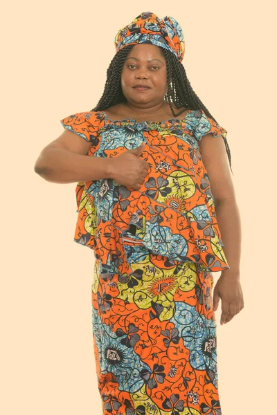 Studio colpo di grasso nero africano donna in piedi mentre indossa abiti tradizionali e dando pollice in su — Foto Stock