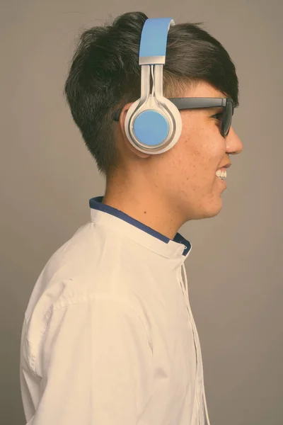Jovem adolescente asiático ouvindo música contra fundo cinza — Fotografia de Stock