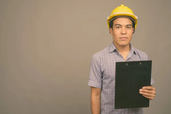 Young Asian businessman wearing hardhat against gray background — Stock Photo, Image