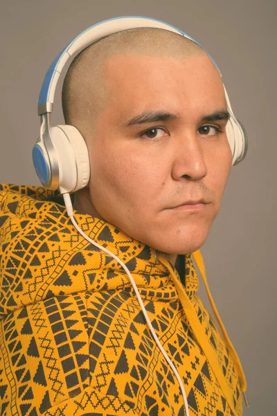 Jong kaal aziatisch man luisteren naar muziek tegen grijs achtergrond — Stockfoto