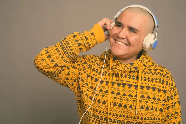 Young bald Asian man listening to music against gray background — Stock Photo, Image