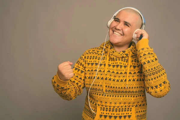 Jovem careca Asiático homem ouvindo música contra fundo cinza — Fotografia de Stock