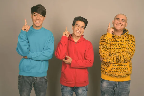 Tři mladí asijští muži nosí teplé oblečení na šedém pozadí — Stock fotografie