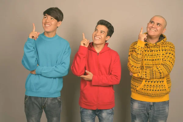 Drei junge asiatische Männer in warmer Kleidung vor grauem Hintergrund — Stockfoto