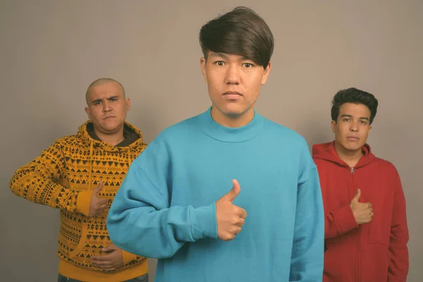 三个年轻的亚洲男人穿着灰色背景的保暖衣服 — 图库照片